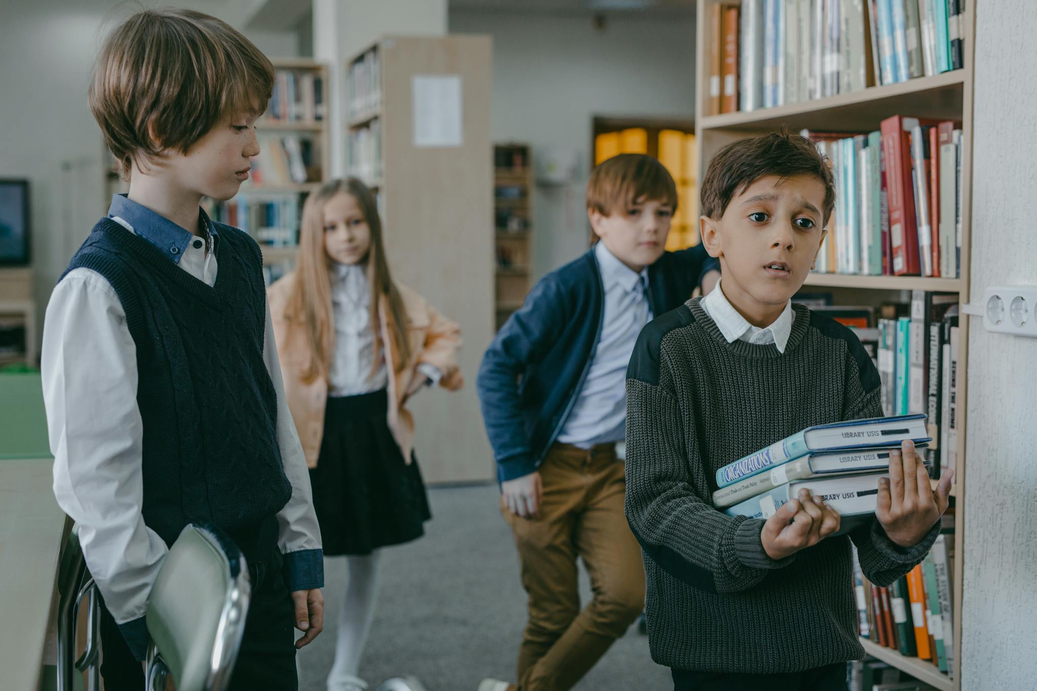 A group of children interacting in a library setting, focusing on a boy holding books.